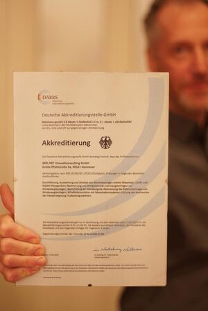Ein Mitarbeiter hält die Akkreditierungsurkunde in die Kamera